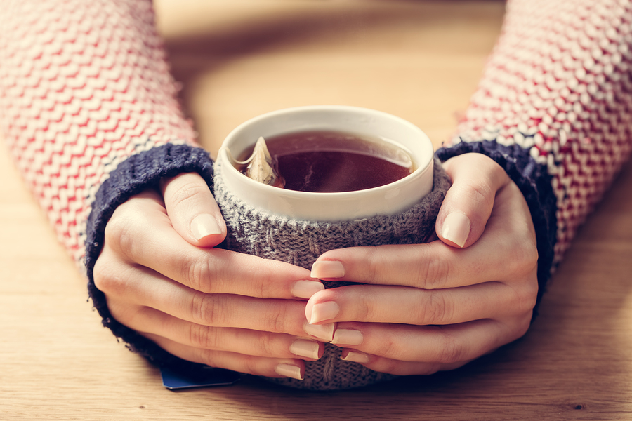 Hot mug of tea warming woman's hands in retro woollen jumper. Wo