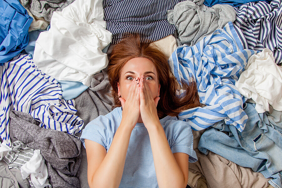 Beautiful caucasian woman smiling and lying down with clutter clothes on the floor.