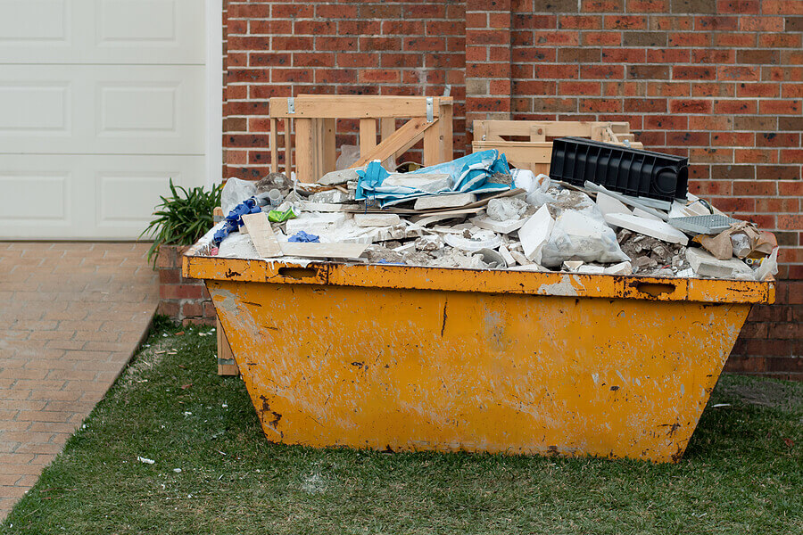 Skip bin container full of household waste rubbish on the front yard. House clean up and renovation concept.