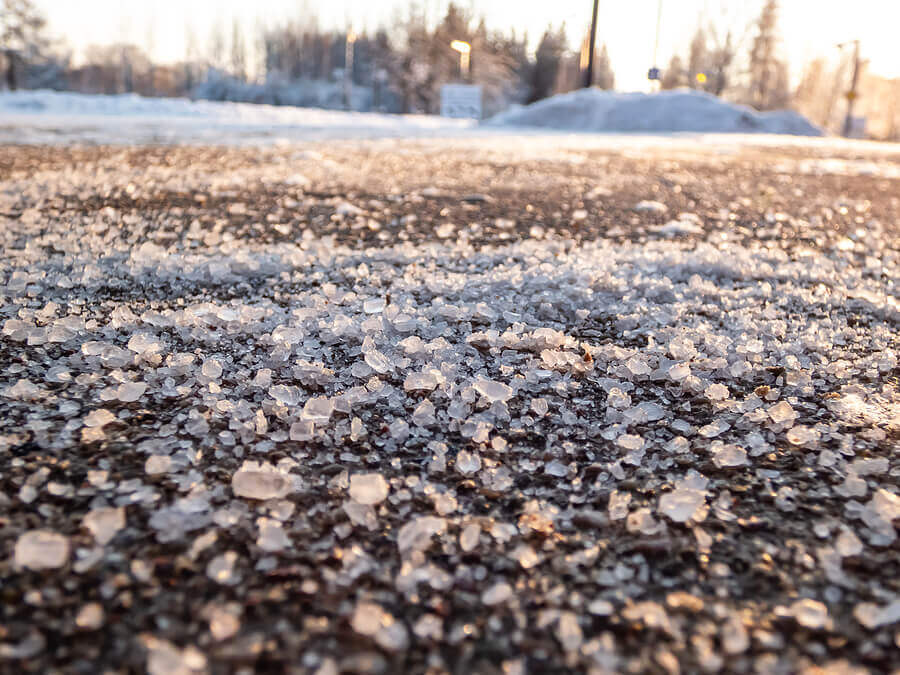 Salt grains on icy sidewalk surface in the winter. Applying salt to keep road clear and people safe in winter weather from ice or snow.