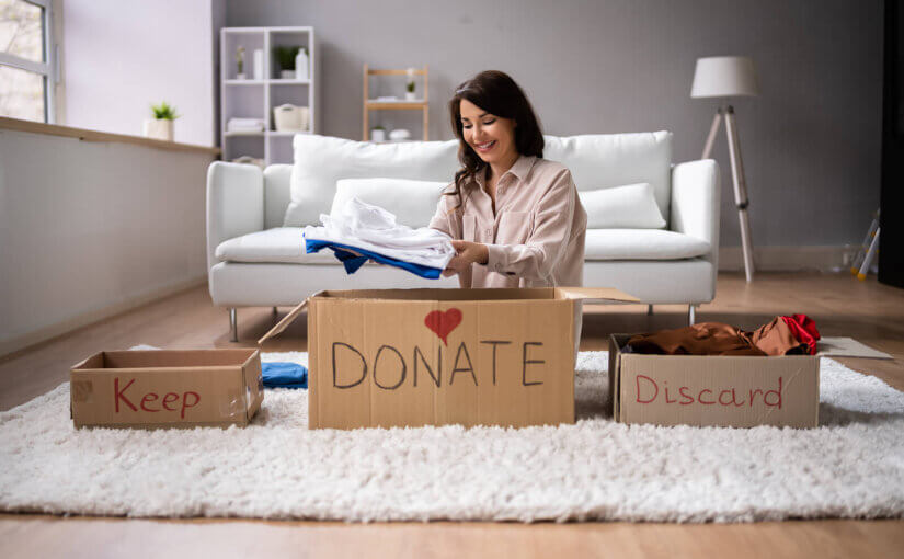A woman sat down, decluttering her house with three boxes: keep, donate, and discard.